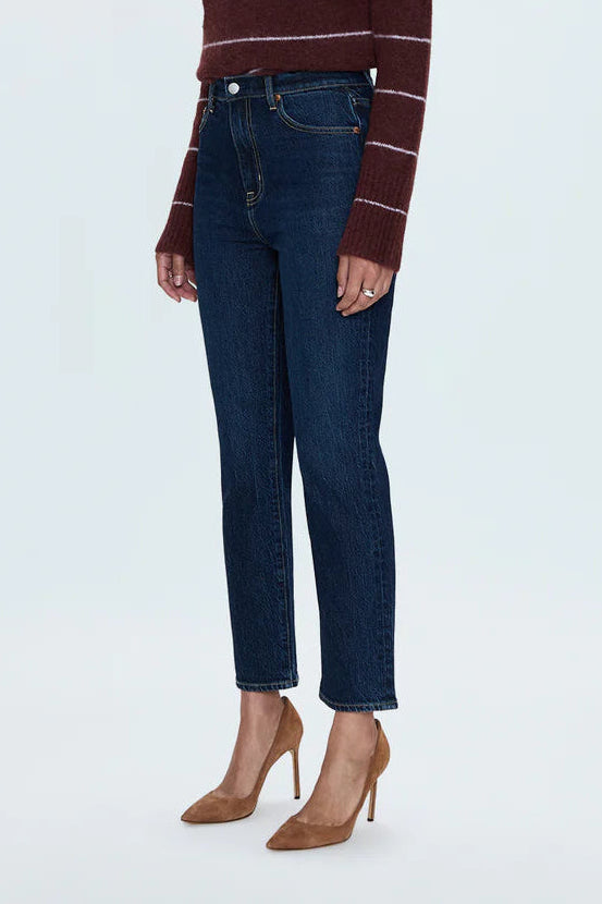 A woman modeling a dark brown and burgundy striped knit sweater paired with dark blue jeans and tan high heels, standing against a light gray studio background.