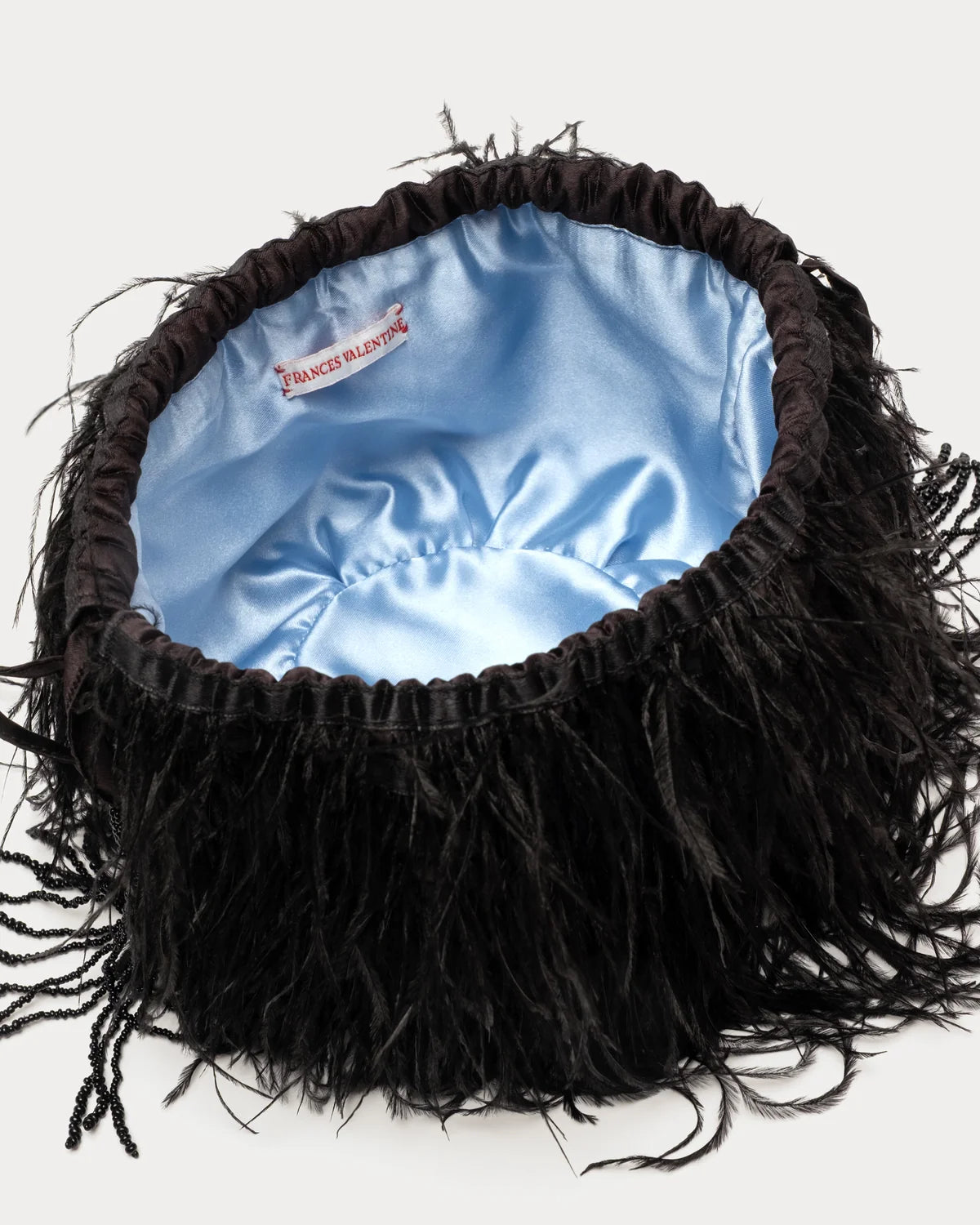 A black feathered fascinator hat with a light blue satin lining, shown from a top-down view on a light gray background.