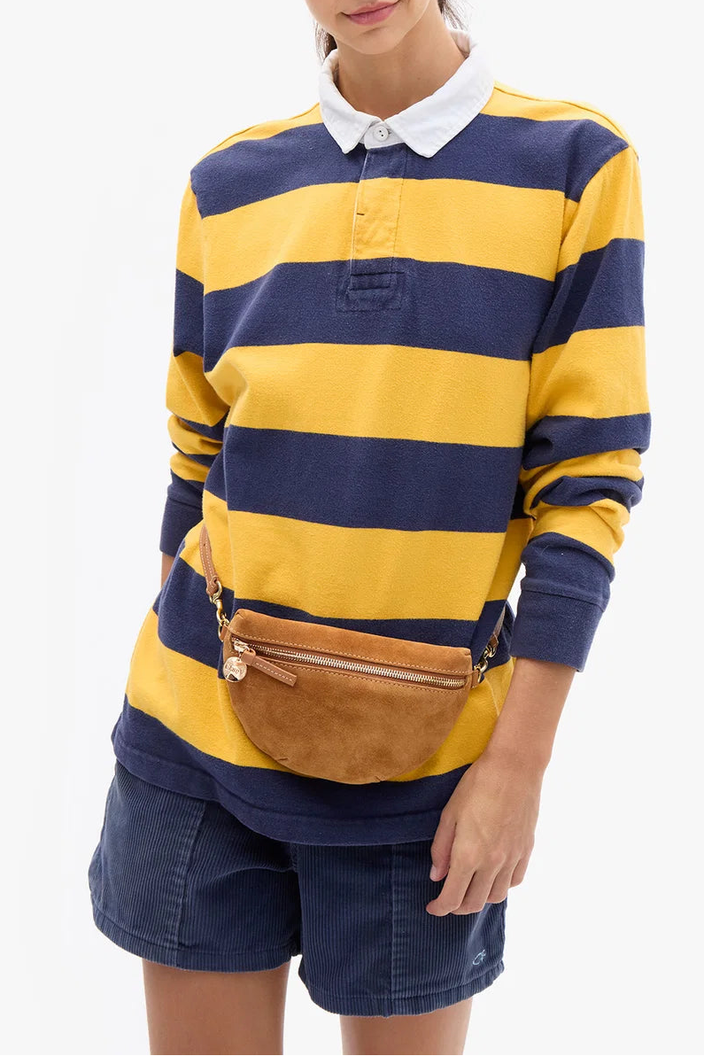 A woman modeling a yellow and navy blue horizontally striped long-sleeve rugby shirt with a white collar, paired with navy shorts and a brown belt bag, against a light gray background.