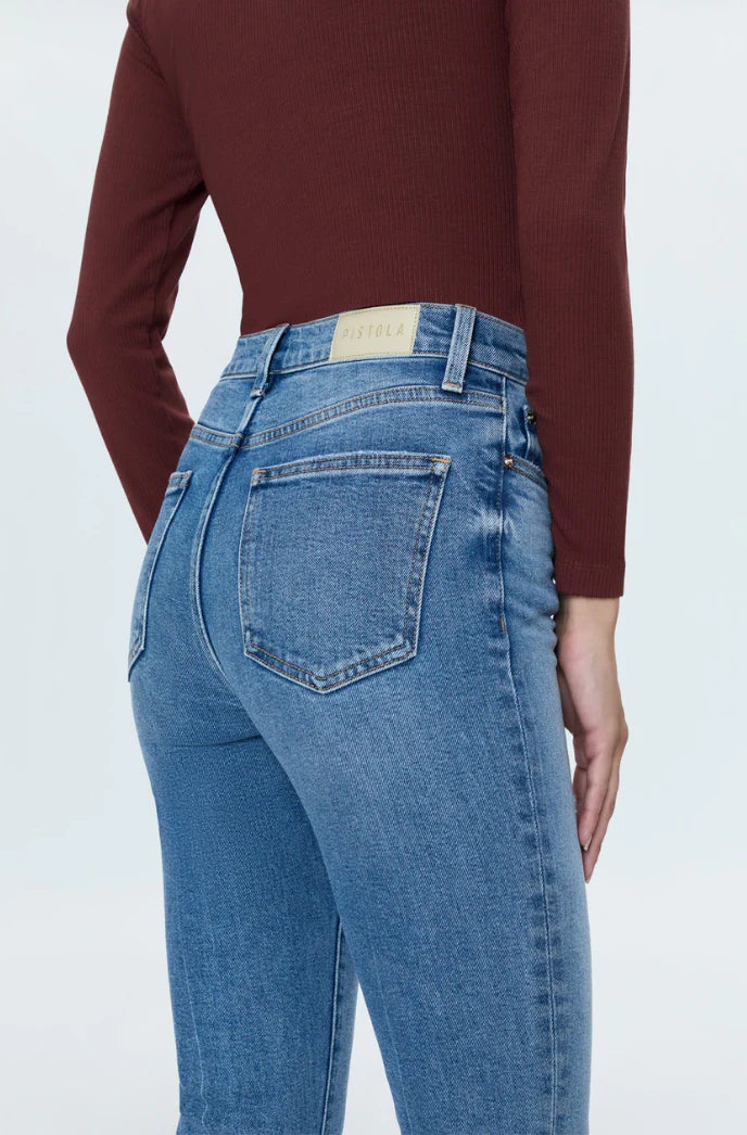 Rear view of a person wearing blue denim jeans and a dark burgundy long-sleeve top against a light gray studio background.