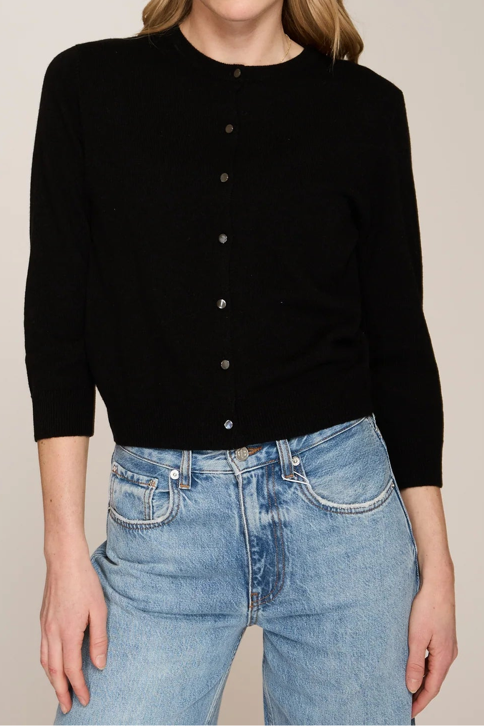 Woman wearing a black cardigan and blue jeans against a beige background