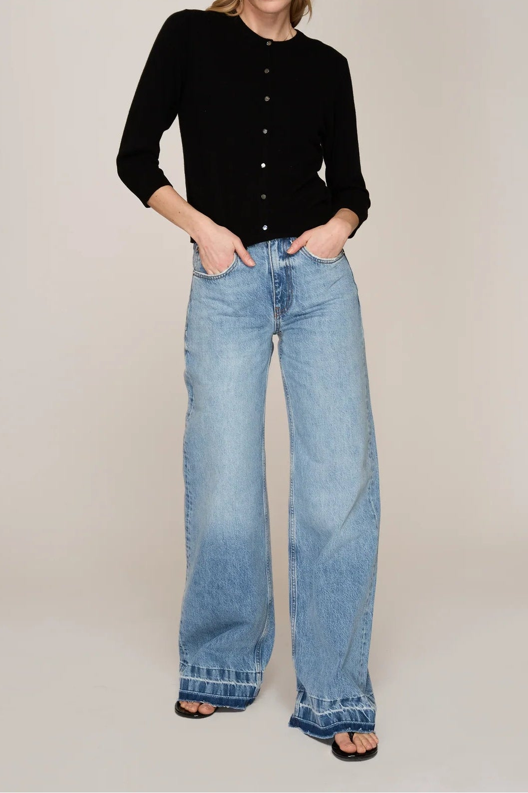 Woman wearing a black cardigan and blue jeans on a plain background