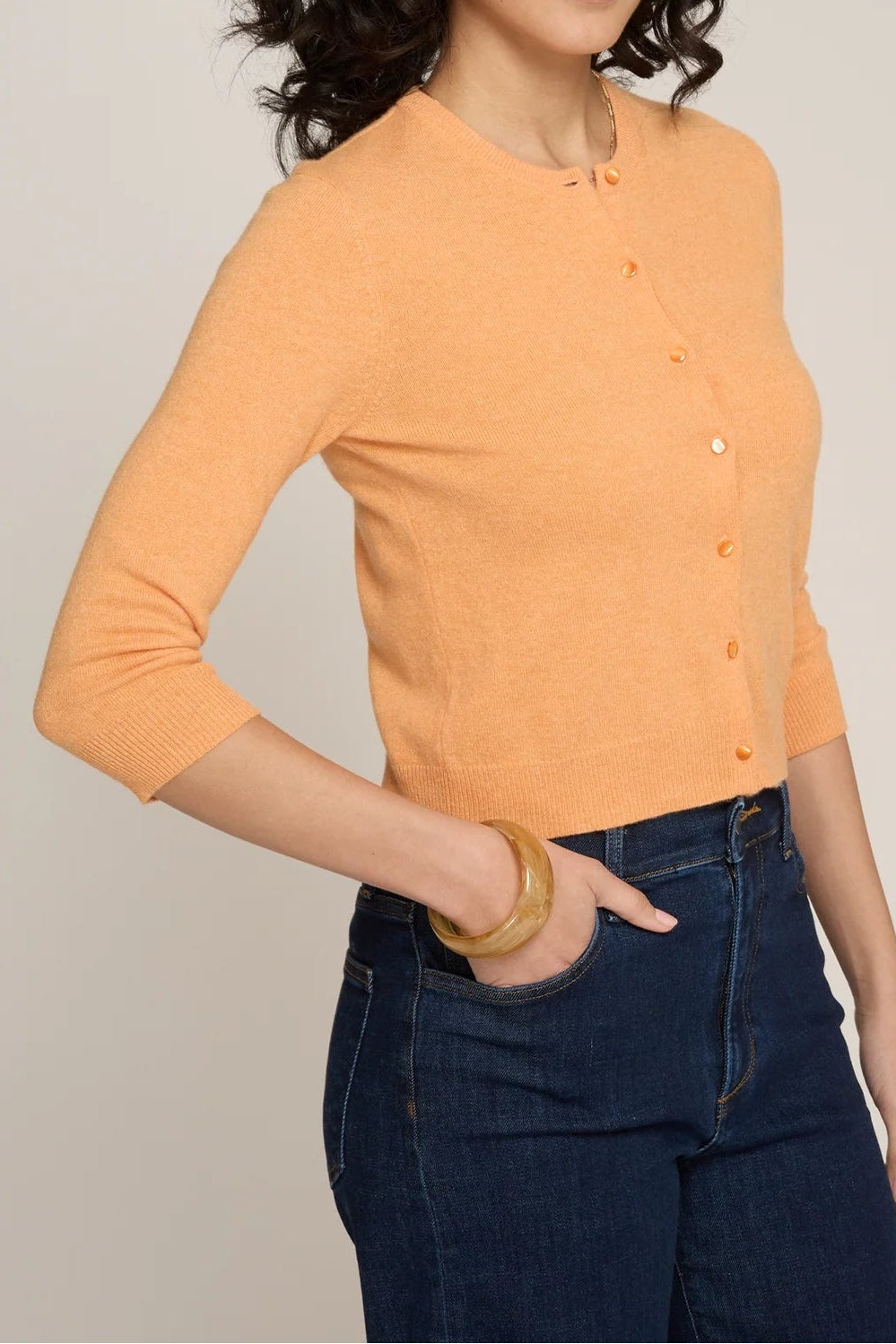Woman wearing an orange cardigan and dark jeans against a plain background