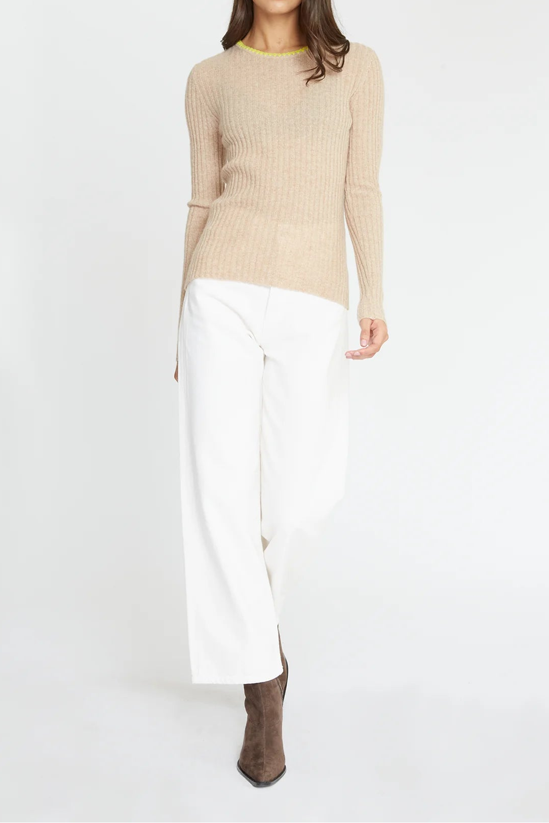 A woman modeling a beige ribbed knit long-sleeve sweater with white wide-leg trousers and brown ankle boots, standing against a plain white studio background.