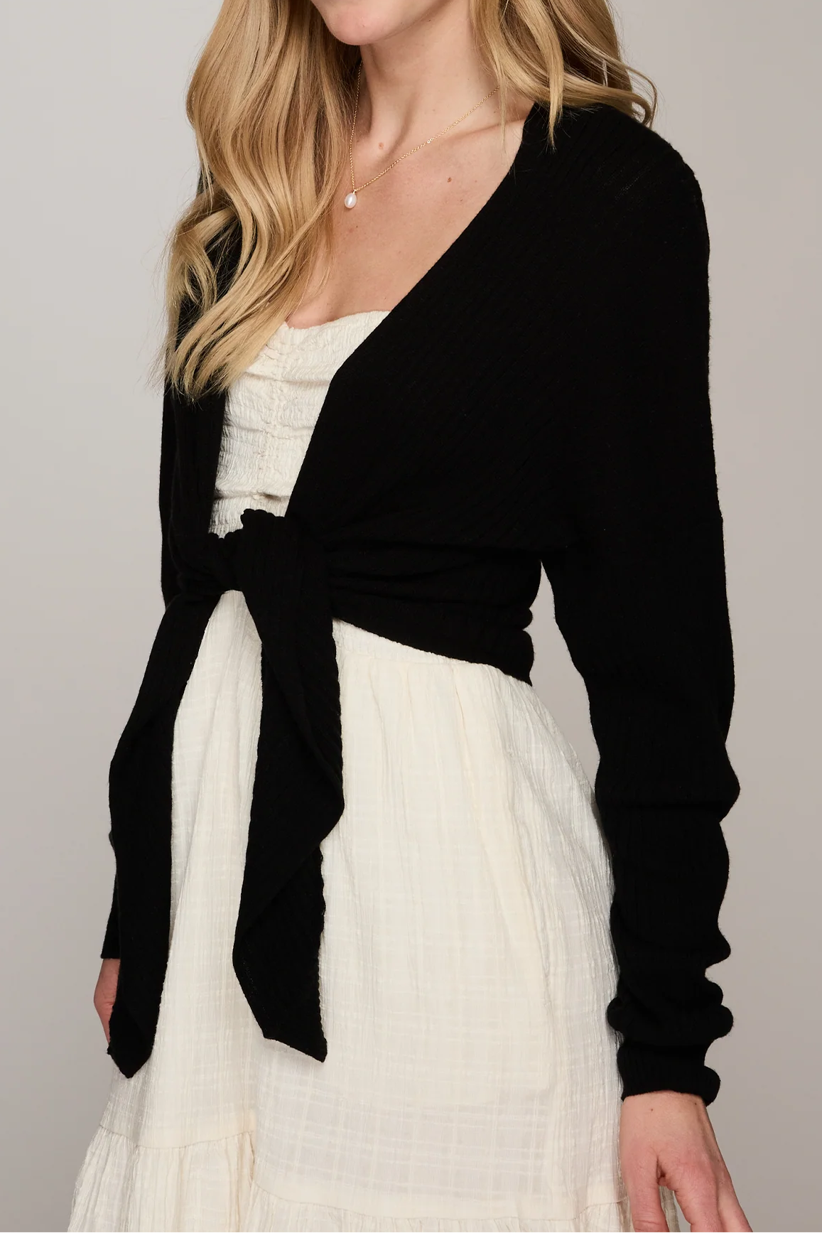 Woman wearing a black cardigan over a white dress against a gray background