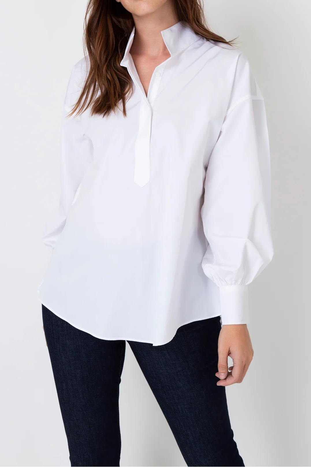 Woman wearing a white shirt and dark pants against a plain background