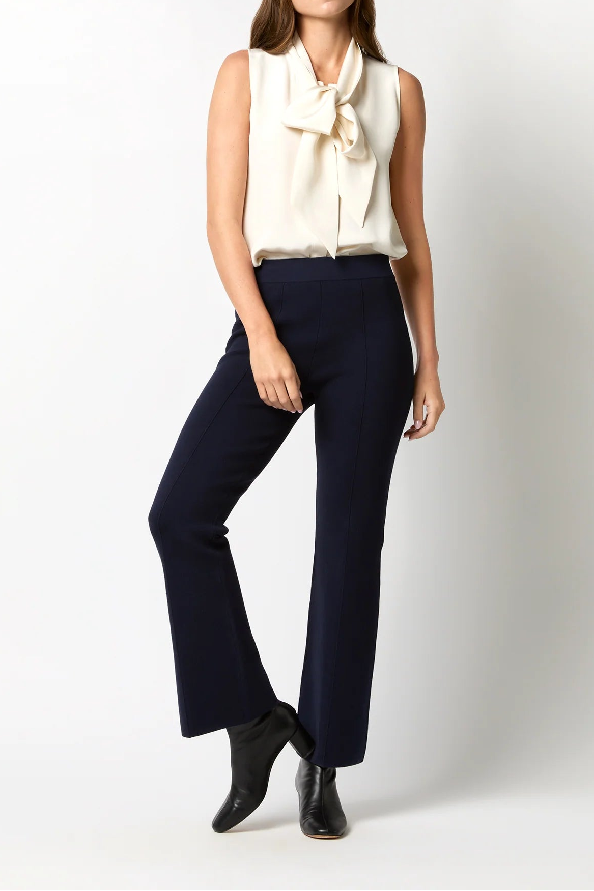 Woman wearing a white sleeveless top with a scarf and dark blue pants on a white background