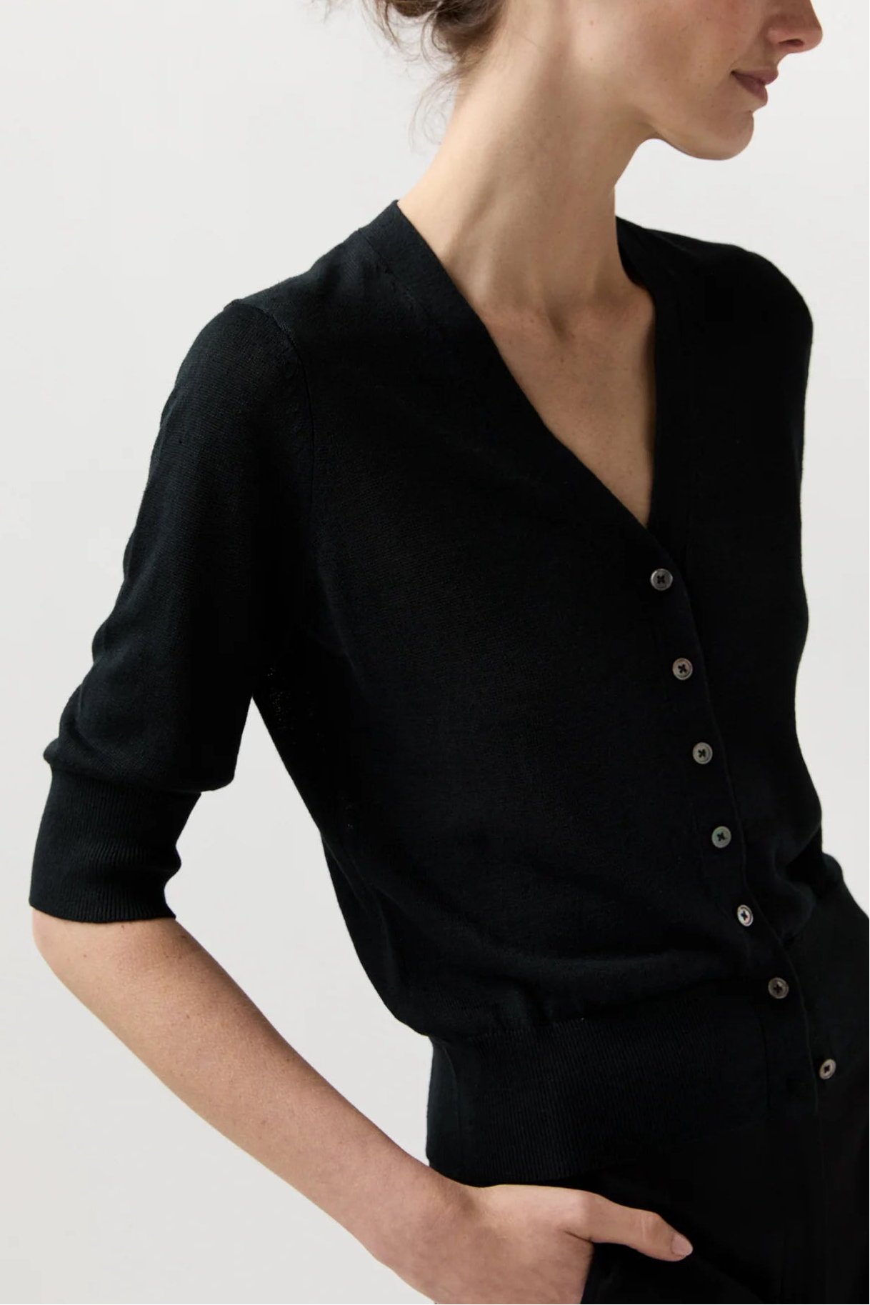 A woman wearing a black knit cardigan with a V-neck and button-front detail, shown in a side profile against a plain light background.