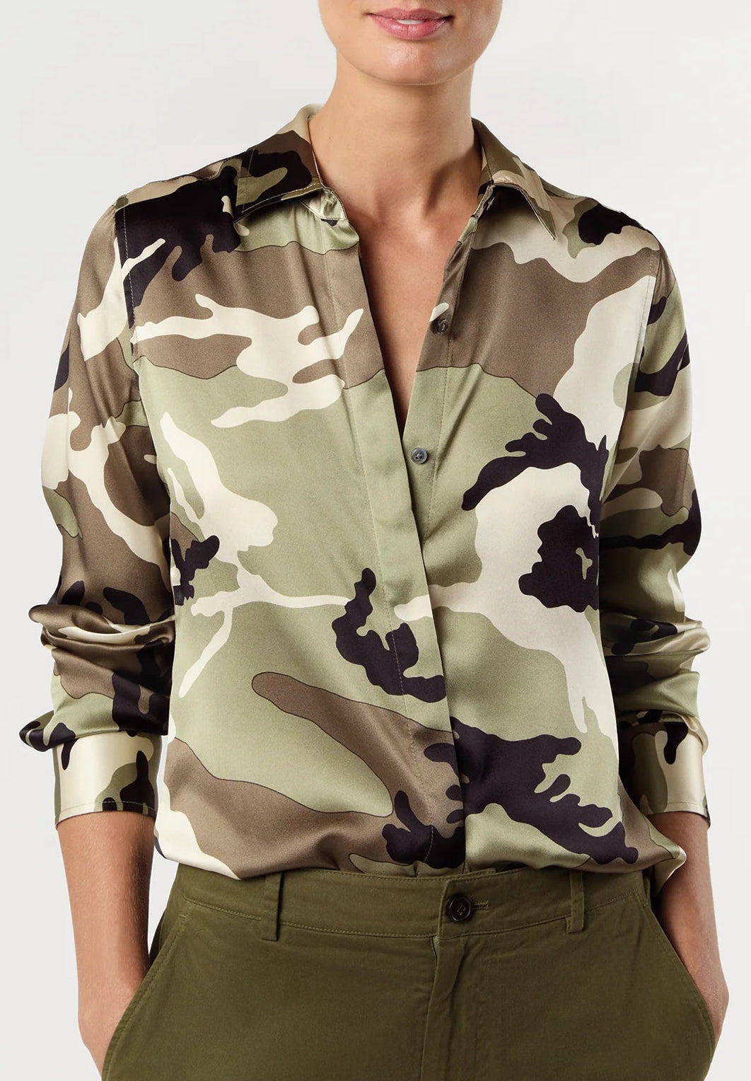 A woman modeling a long-sleeve button-up shirt with an olive green, beige, and black camouflage pattern, paired with olive green trousers, against a plain light gray background.