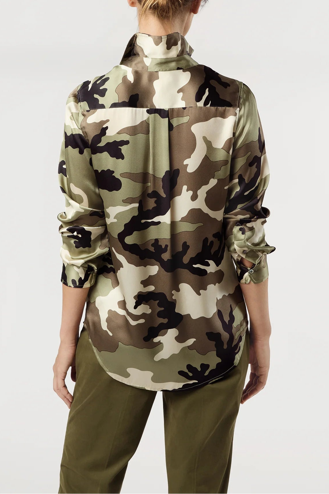 A woman shown from the back wearing a long-sleeve camouflage shirt and olive green pants against a plain light gray studio background.