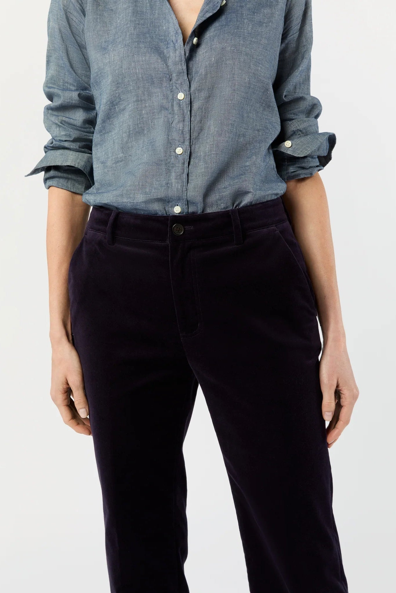 Person wearing a blue button-up shirt and dark pants on a light gray background