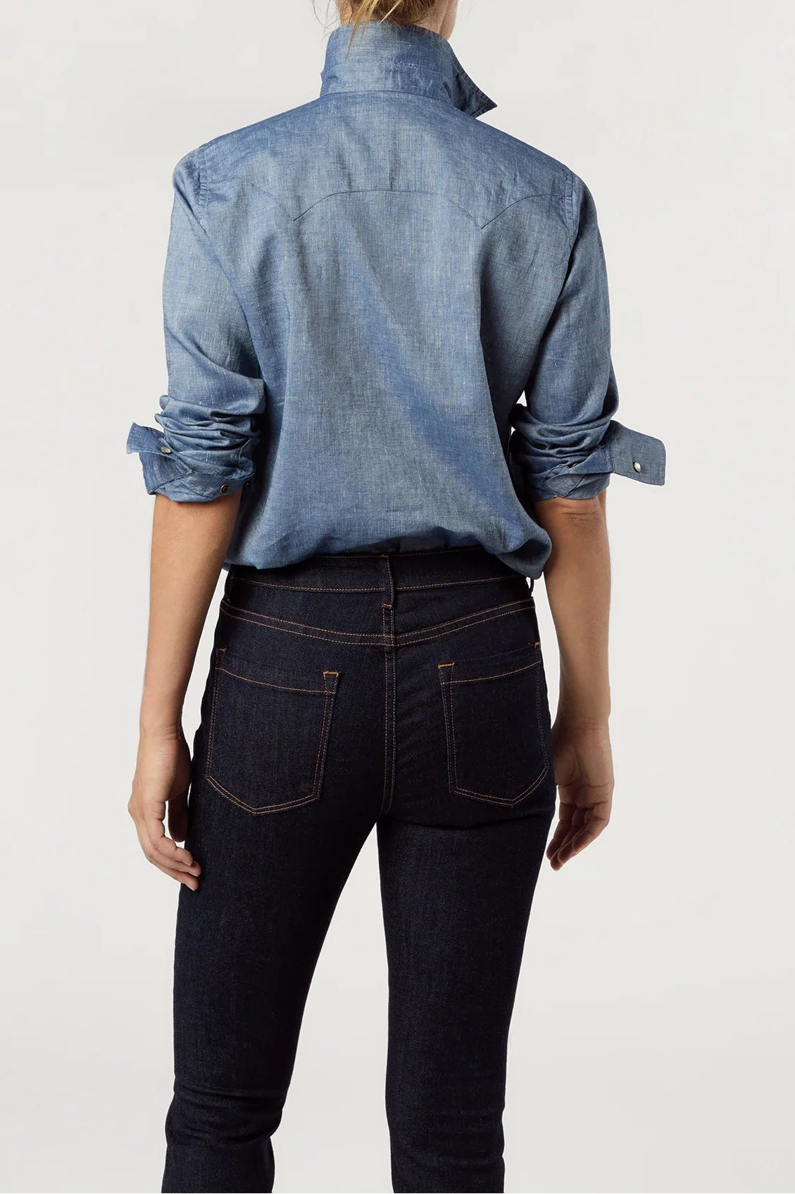 Person wearing a blue denim shirt and dark jeans on a white background