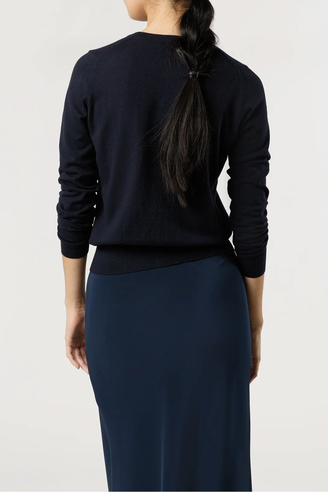 Person wearing a black long-sleeve top and dark blue pants on a white background