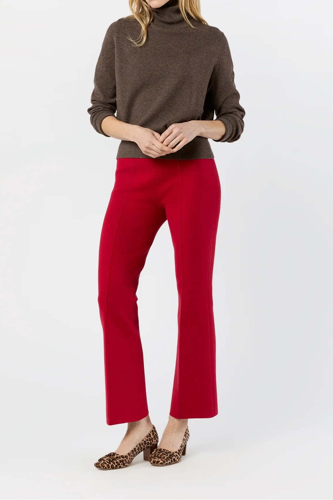 A woman modeling a dark brown ribbed turtleneck sweater and bright red flared pants, paired with leopard-print pointed-toe heels, against a plain white studio background.
