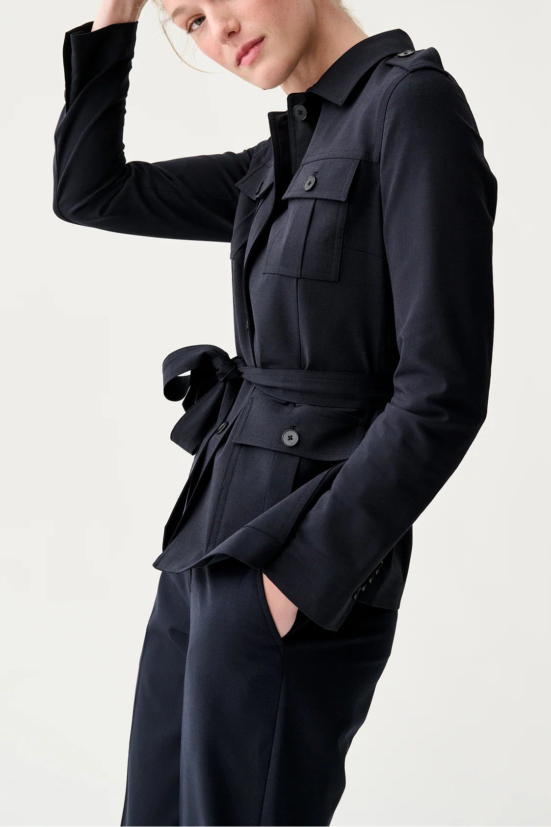 Woman wearing a black outfit with a belt against a light gray background
