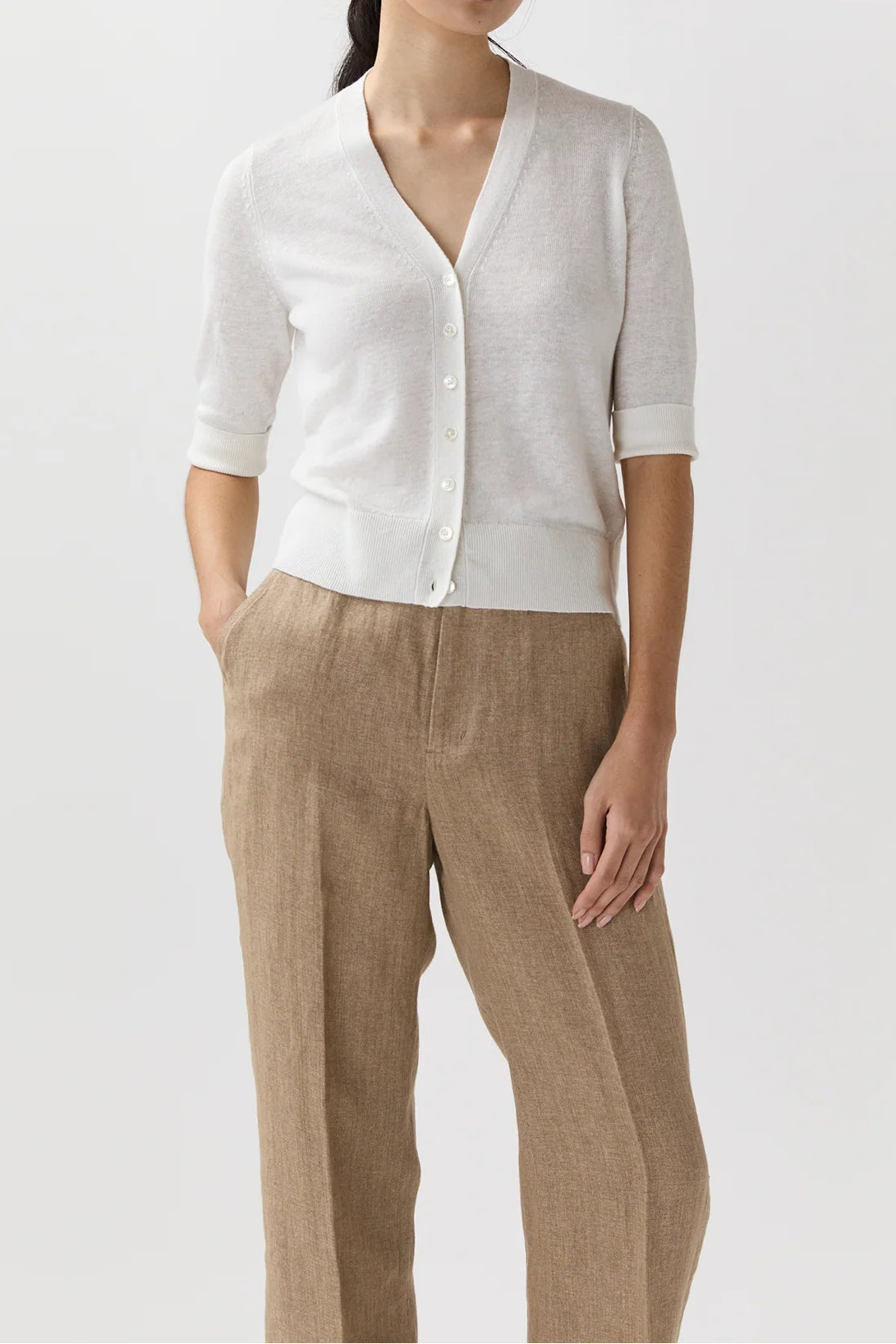 Woman wearing a white cardigan and beige pants on a white background