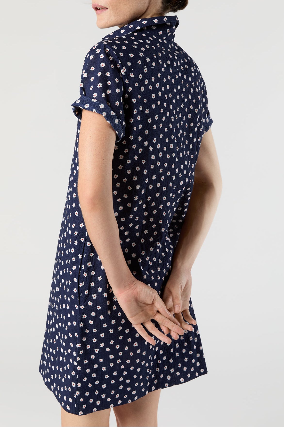 Woman wearing a navy dress with white floral pattern on a light gray background