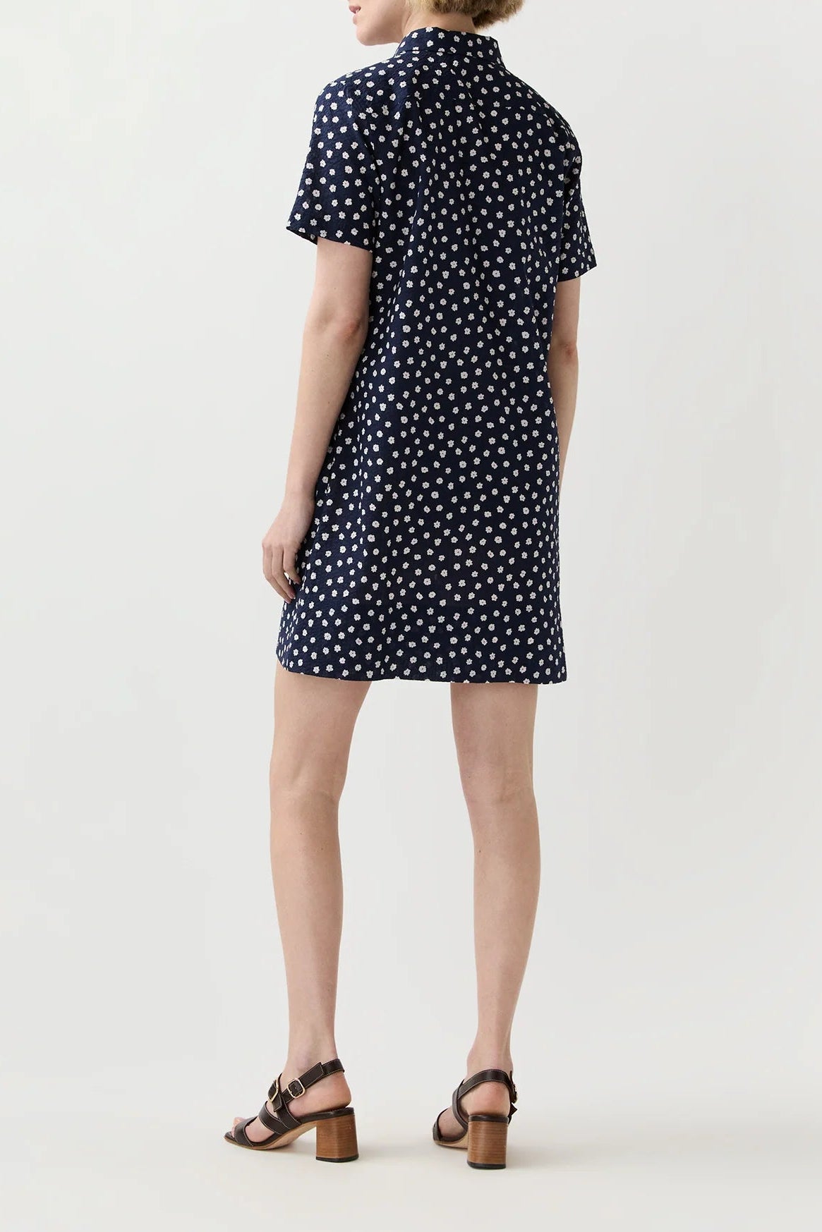 Woman wearing a navy dress with white polka dots on a plain background