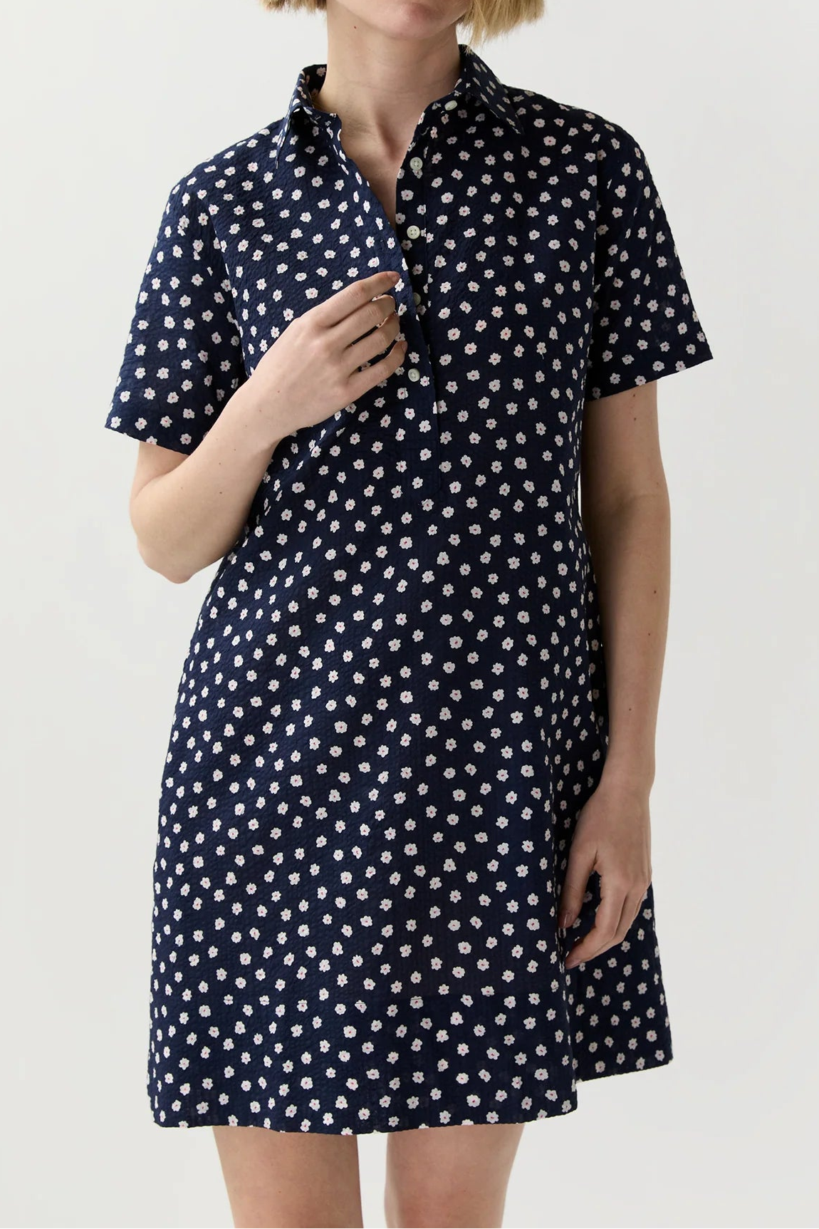 Woman wearing a navy dress with white polka dots on a light gray background