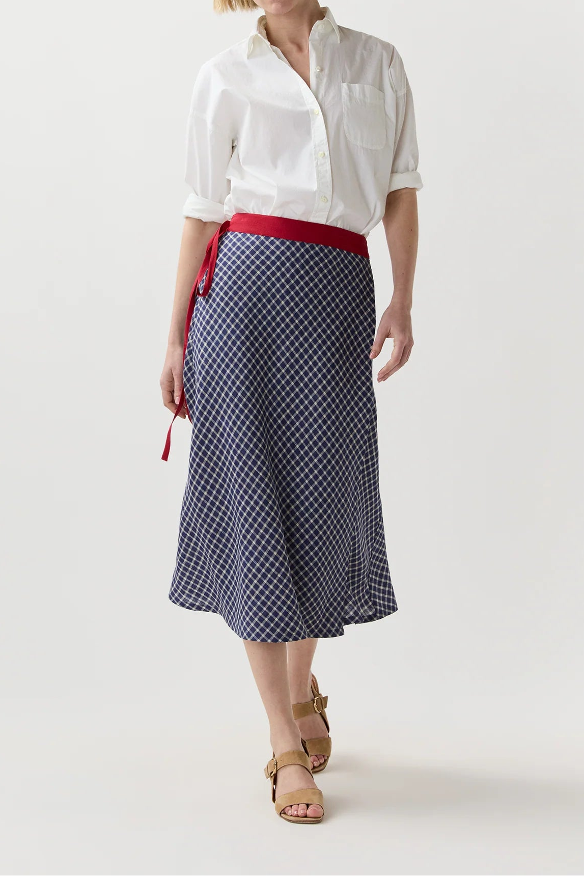A woman modeling a white short-sleeve button-up shirt and a navy blue midi skirt with a small white geometric pattern, cinched at the waist by a red belt.