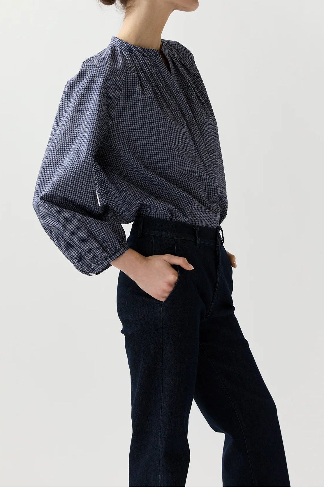 Woman wearing a blue checkered blouse and black pants on a white background