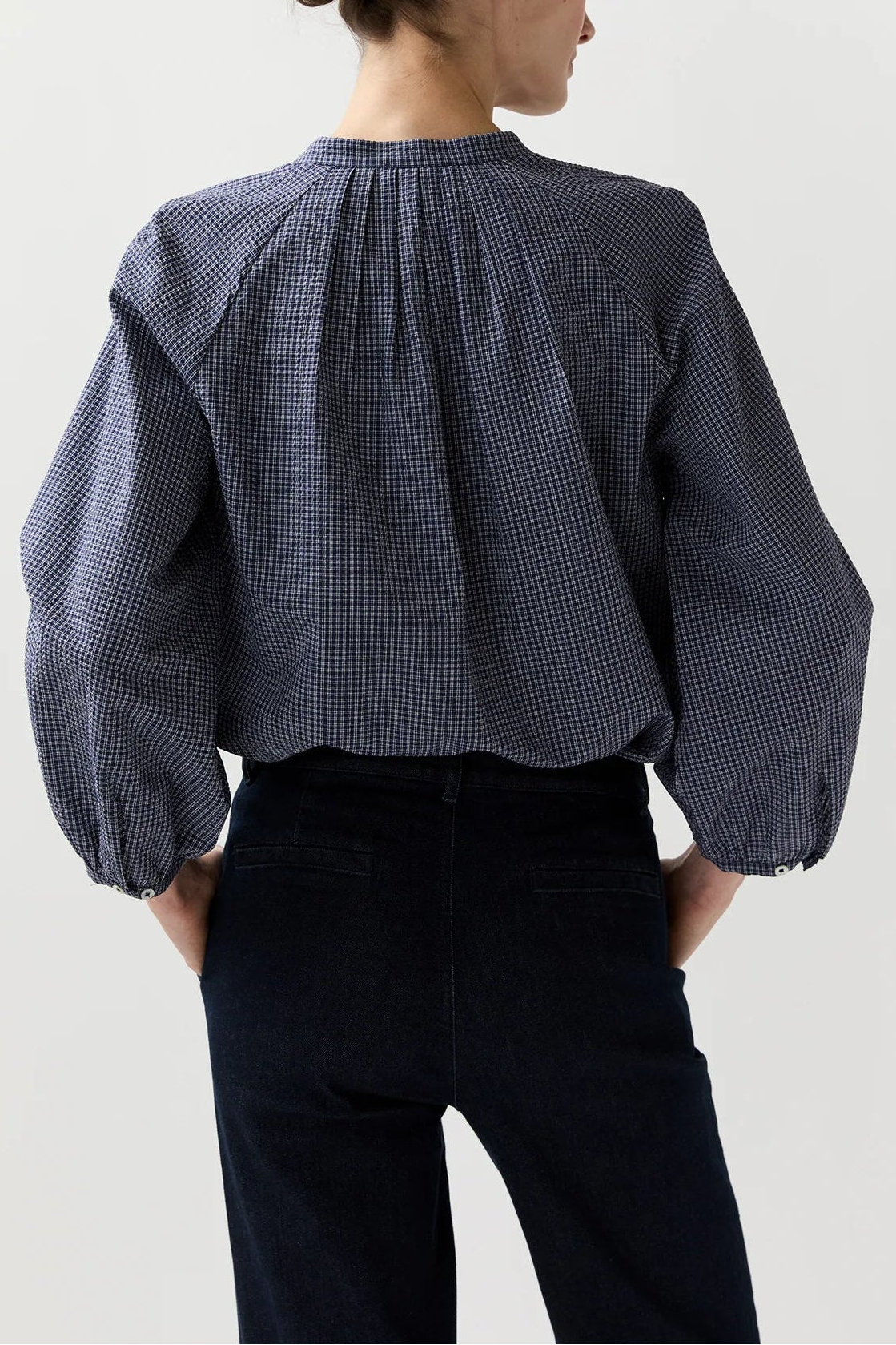 Person wearing a blue checkered shirt with puffed sleeves on a white background