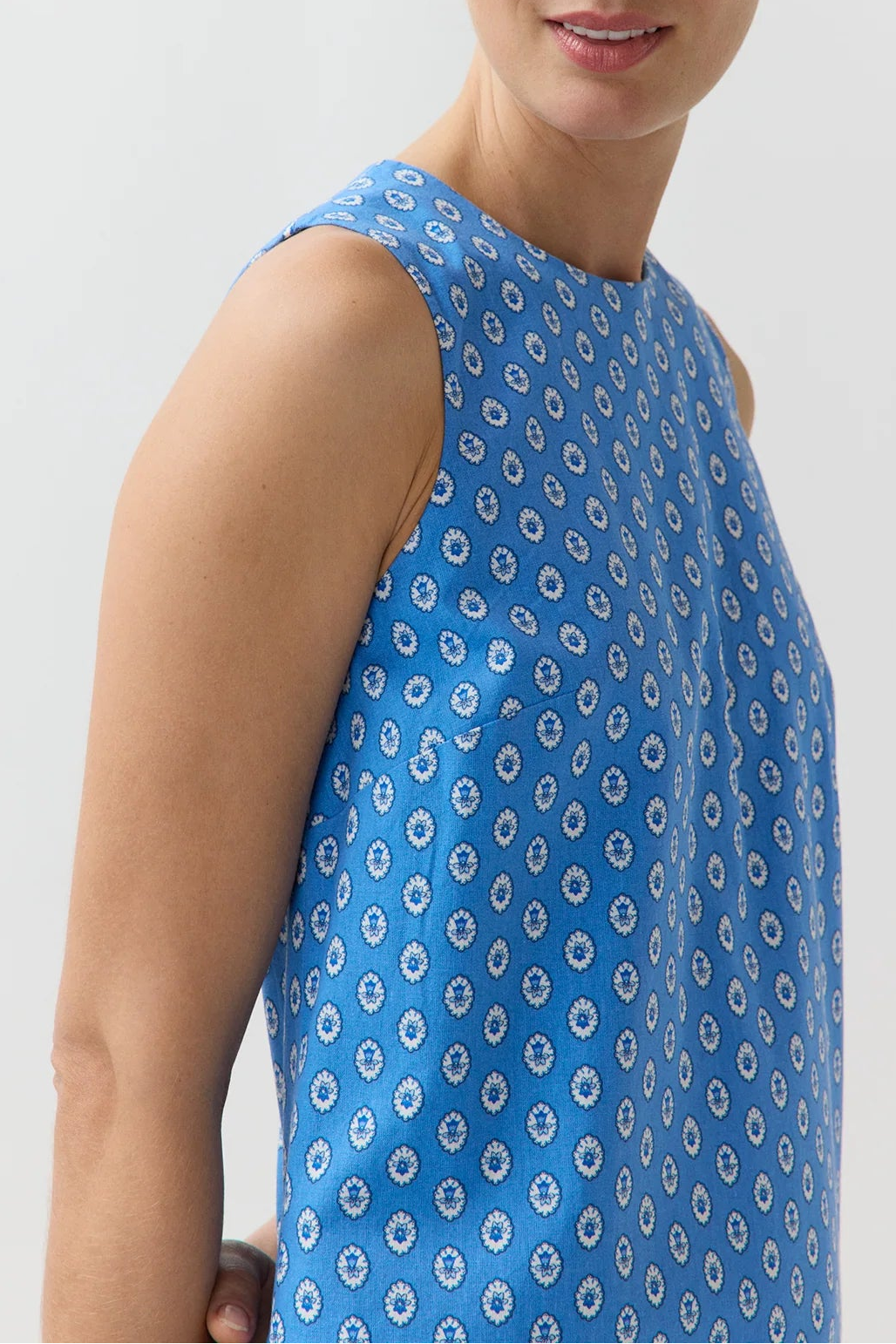 Woman wearing a blue sleeveless dress with a pattern on a plain background