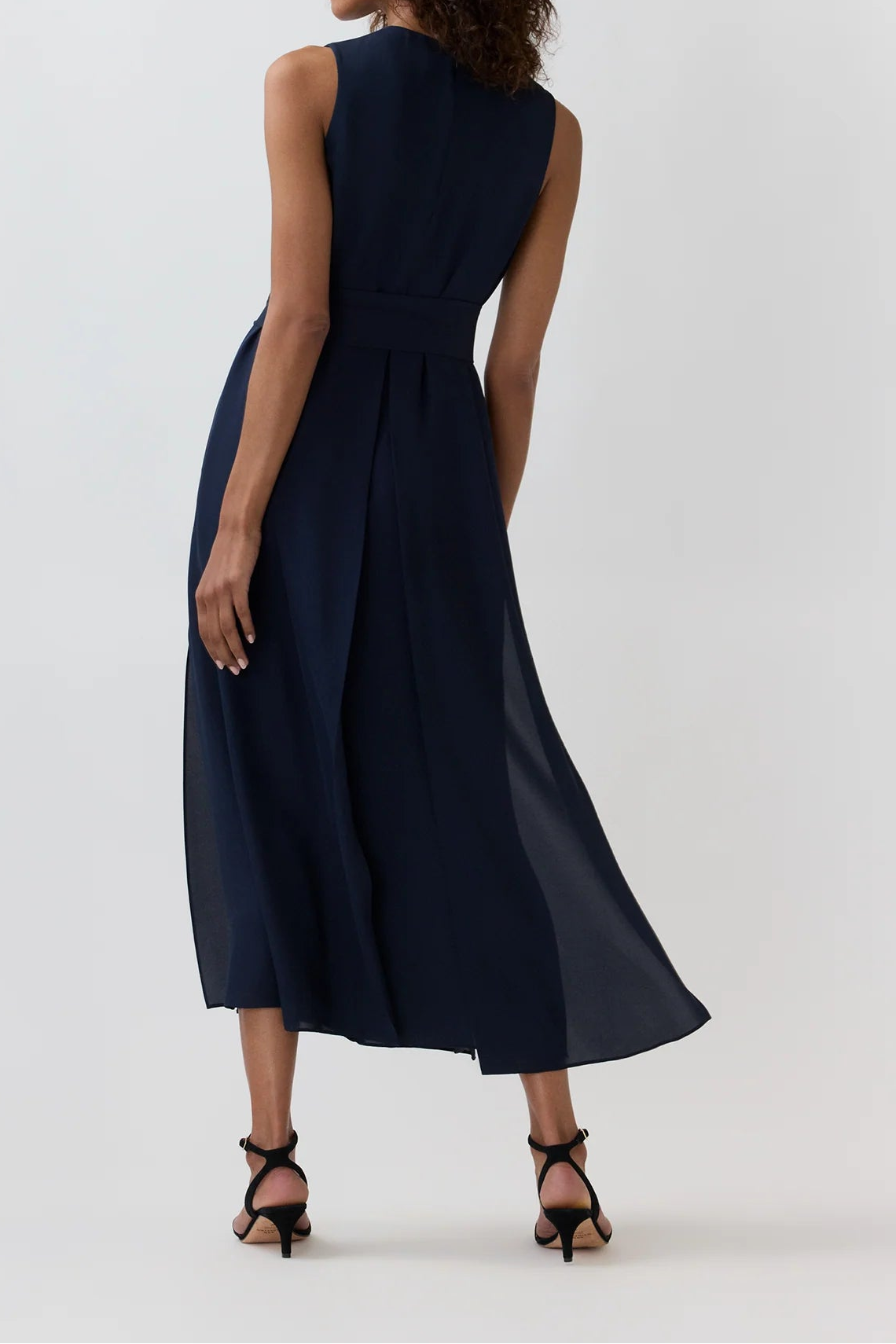 A woman wearing a sleeveless navy midi dress, shown from the back against a plain white studio background.