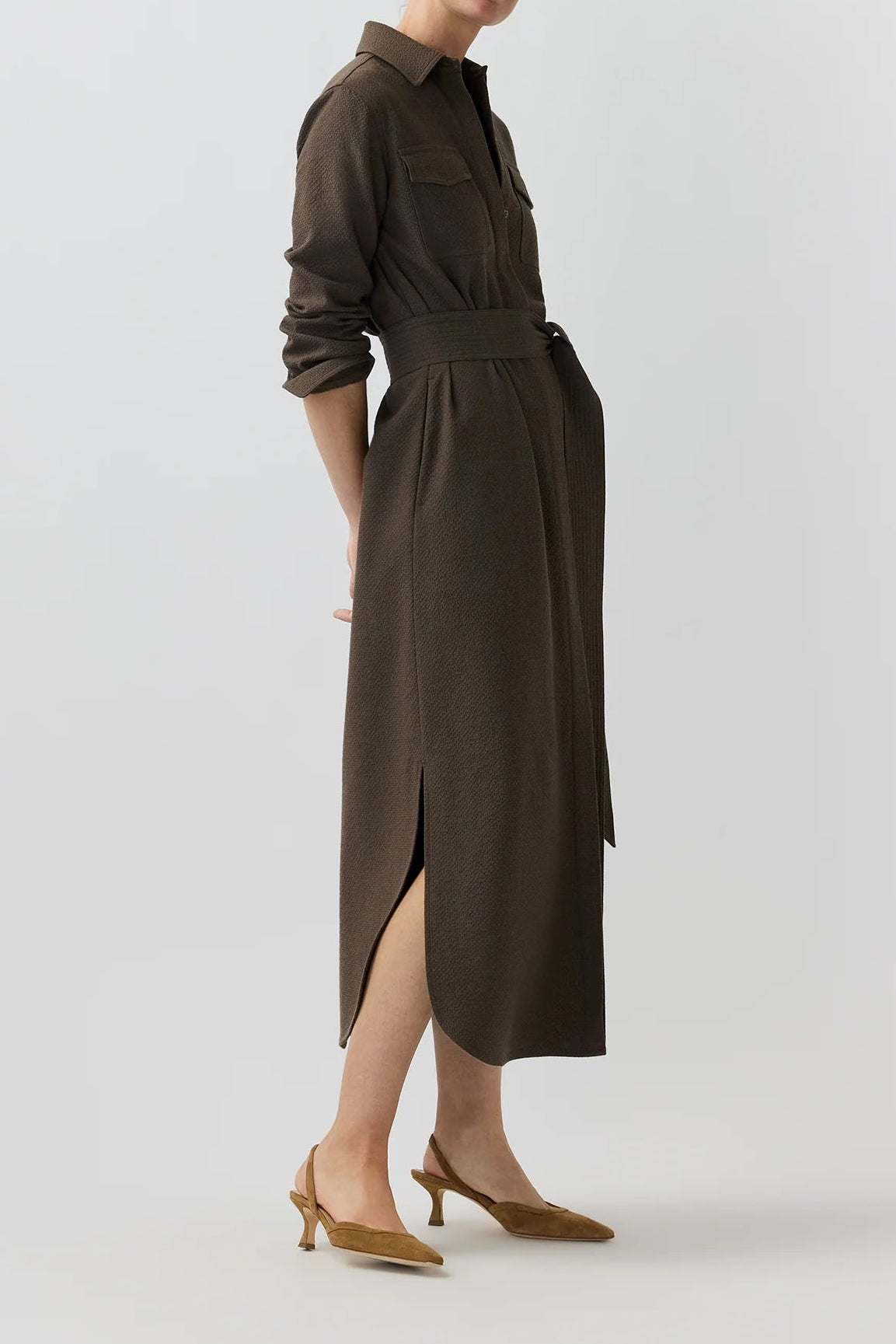 A woman modeling a dark brown long-sleeve midi shirt dress with a matching belt, shown in profile against a light gray studio background.
