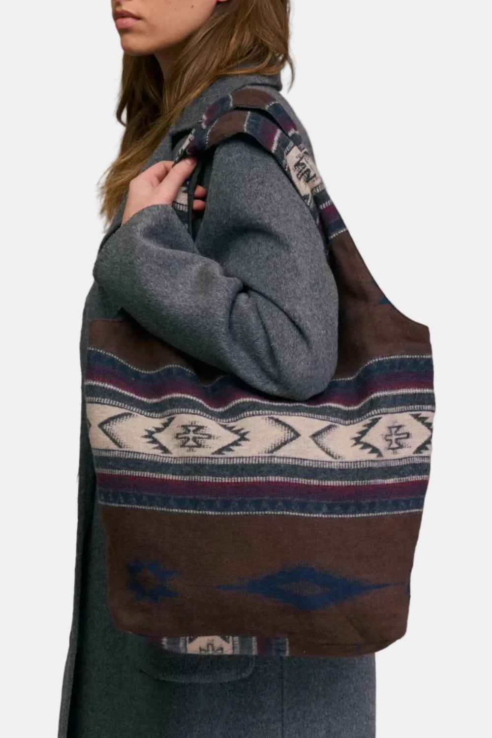 Person wearing a gray coat with a patterned brown bag over their shoulder against a beige background
