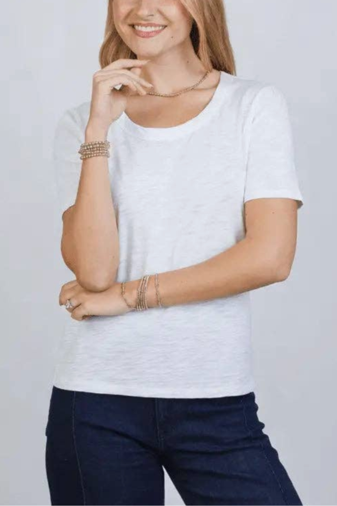 Woman wearing a white t-shirt and dark pants against a light gray background