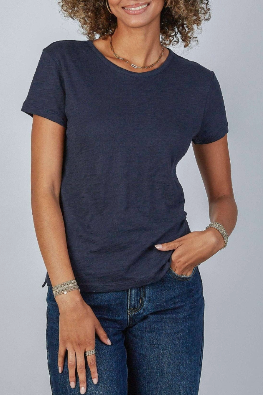 Woman wearing a navy blue t-shirt and jeans against a gray background