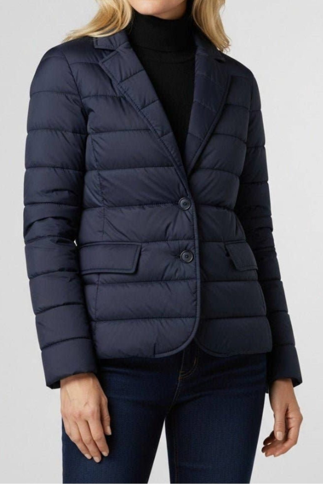 Woman wearing a navy puffer jacket on a light gray background