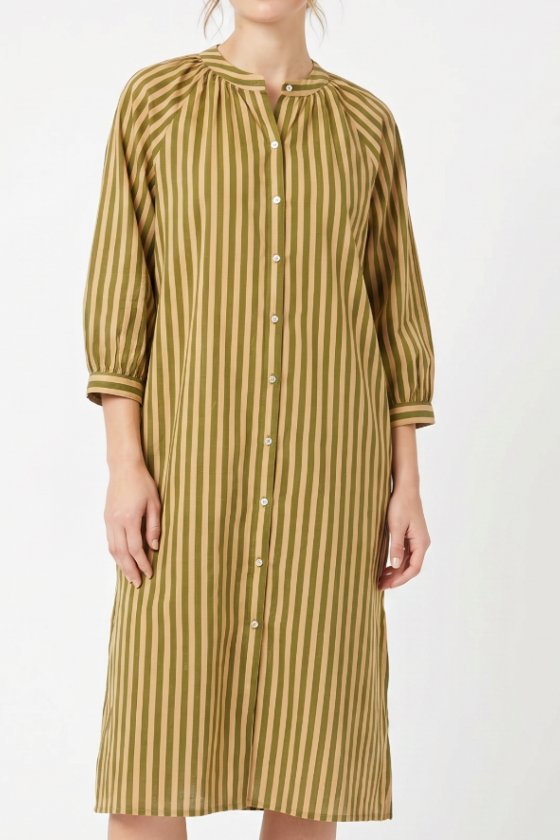 A woman wearing a long-sleeved button-front dress with vertical olive green and beige stripes, photographed against a plain light gray studio background.