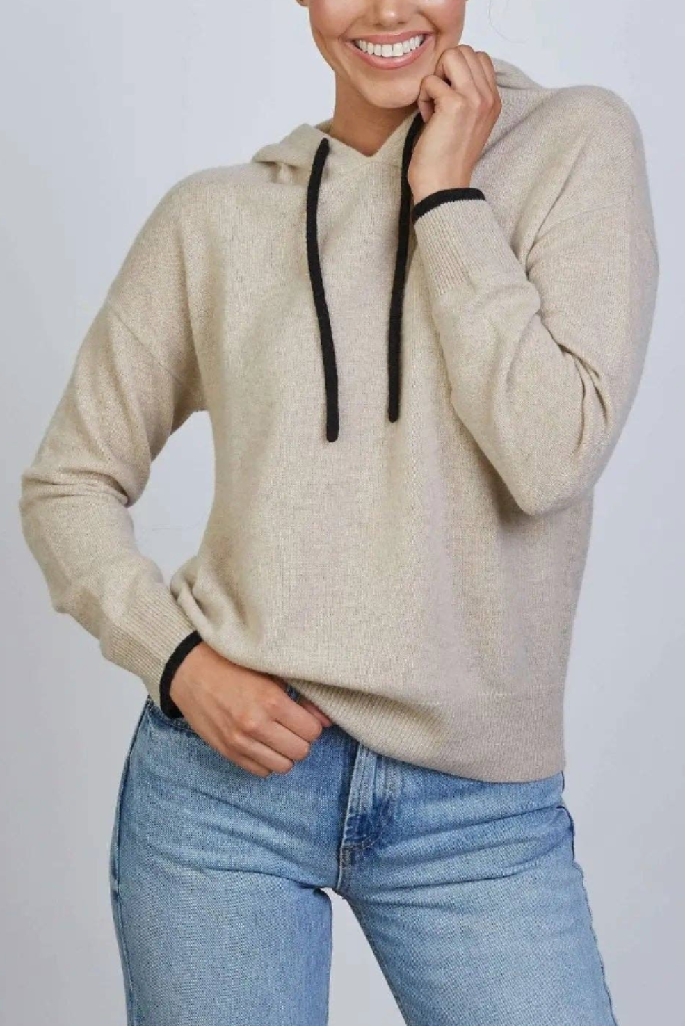 Woman wearing a beige hoodie and blue jeans against a plain background