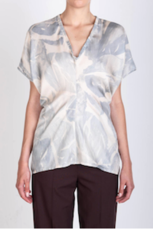 Person wearing a patterned blouse with short sleeves on a plain background
