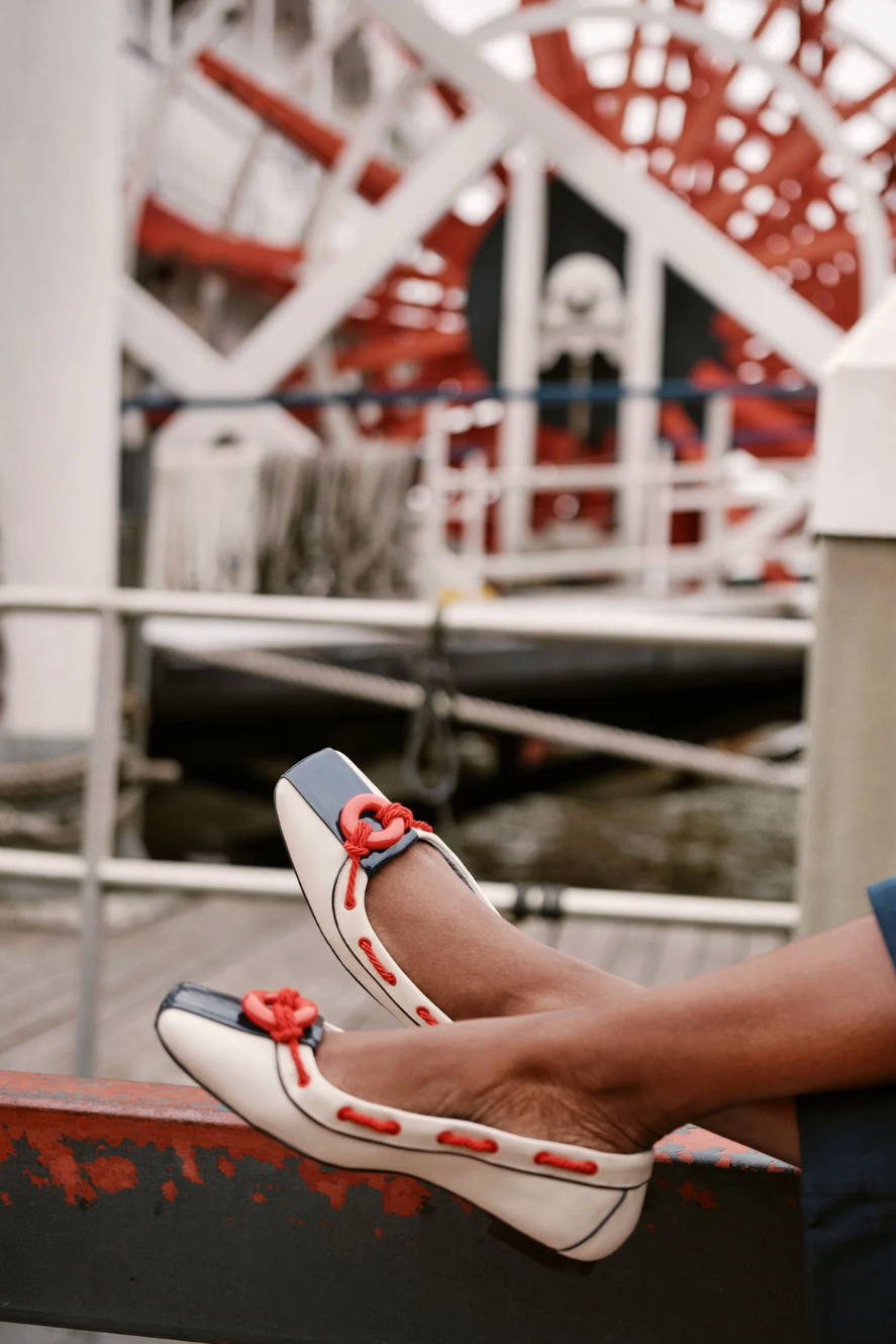 White shoes with red accents on a dock with a paddle wheel in the background