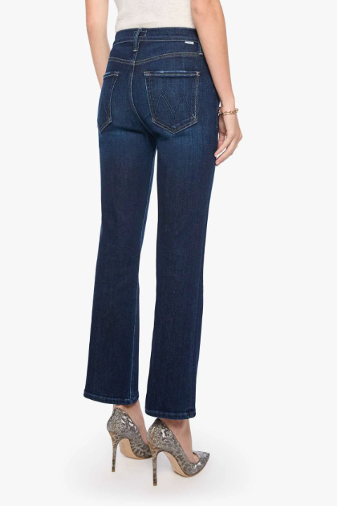 Rear view of a model wearing dark blue flare jeans, a light beige top, and patterned high heels against a plain white background.