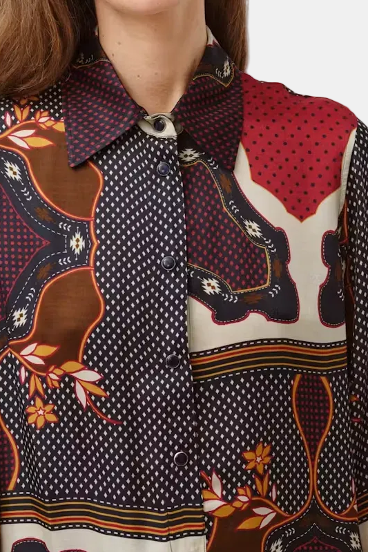 A close-up of a woman wearing a long-sleeve button-up shirt with a complex multicolor print featuring navy, red, brown, and cream patterns.