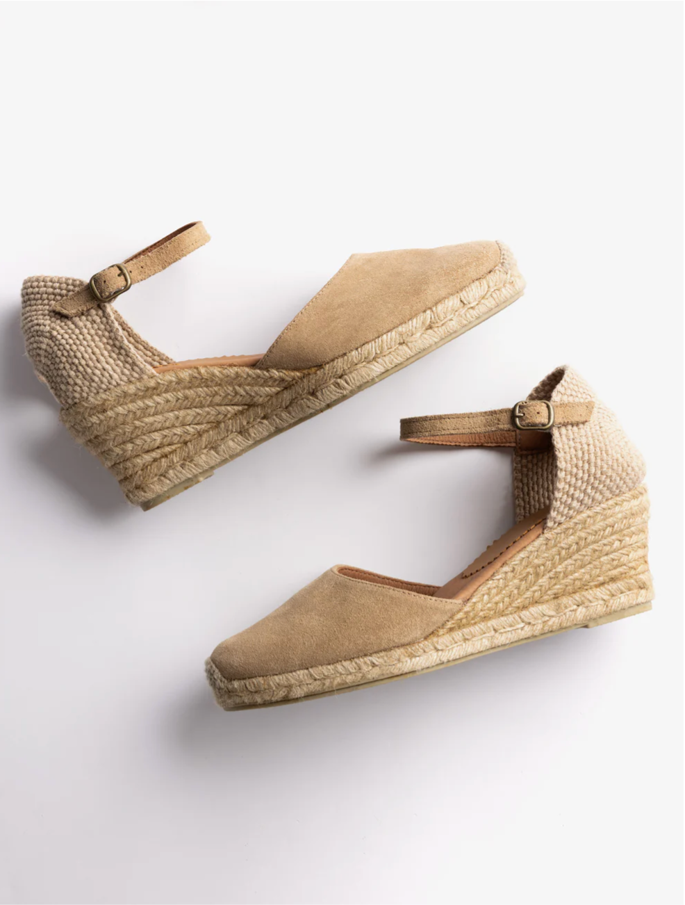 A pair of beige wedge espadrilles with woven jute soles and adjustable ankle straps, displayed on a clean white background.