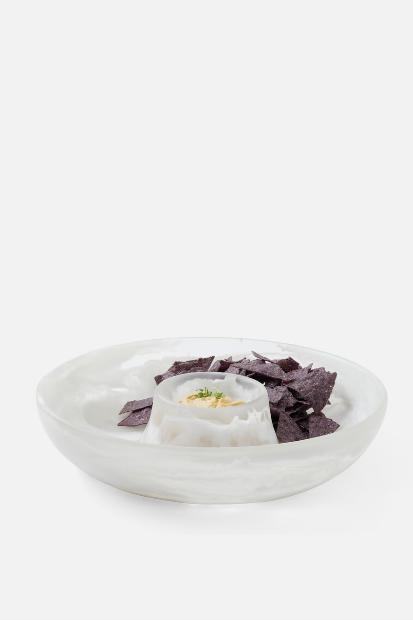 White bowl with tortilla chips and a small container of dip on a white background