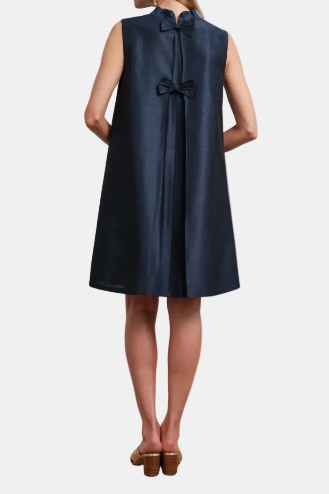 Woman wearing a navy sleeveless dress with a bow detail on a white background