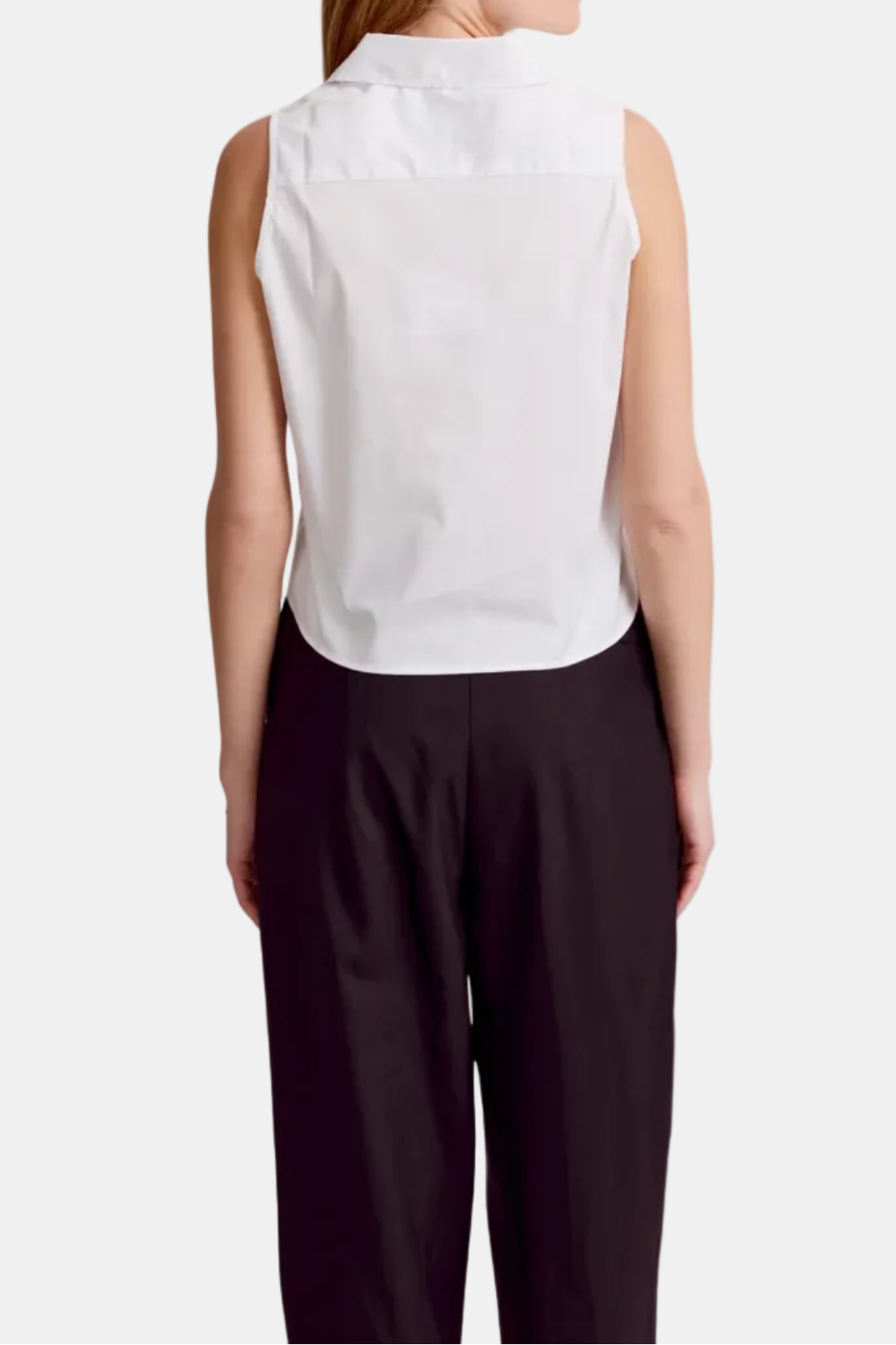 A woman shown from the back wearing a sleeveless white collared blouse and dark pants against a plain white background.
