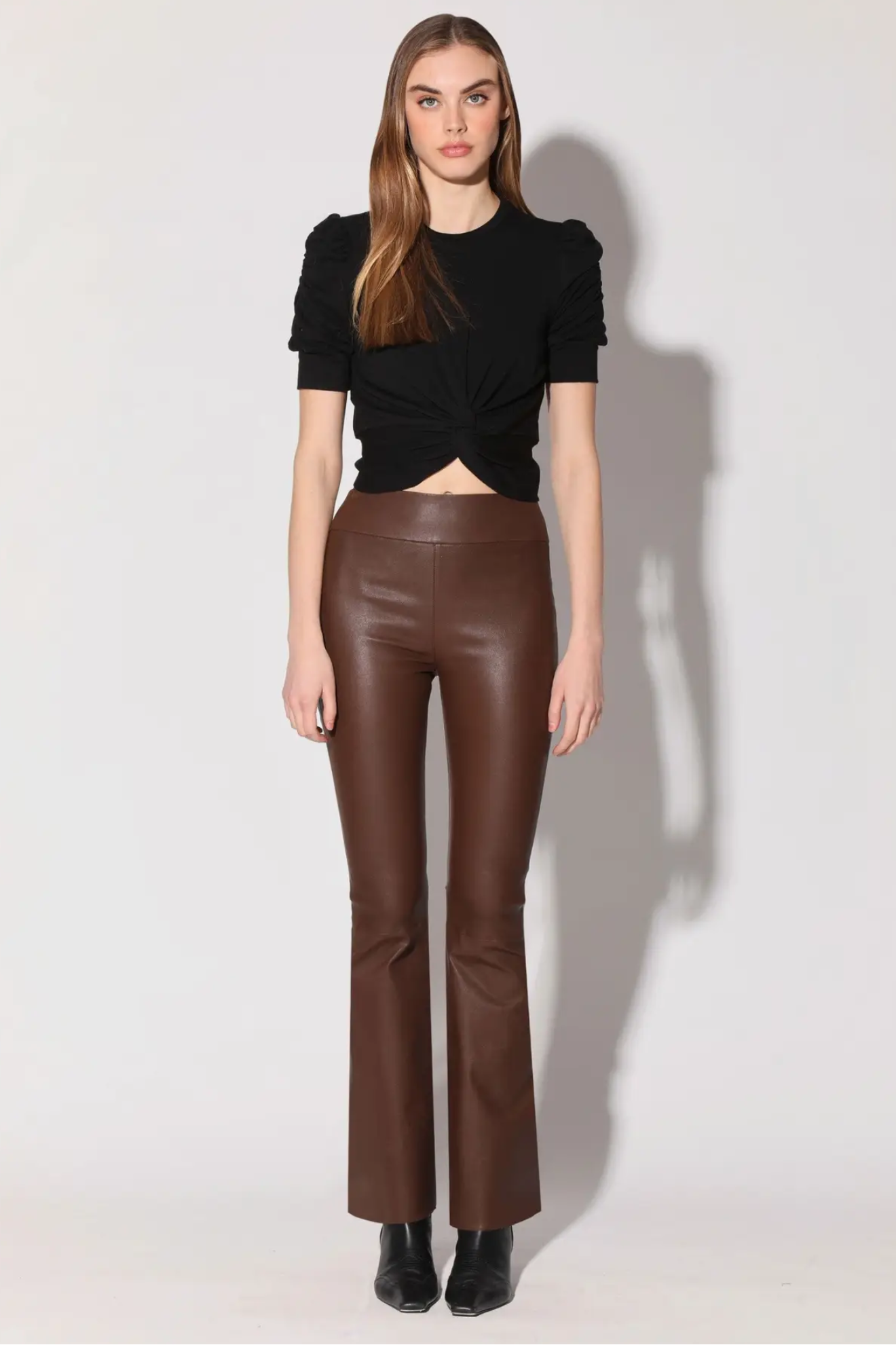 Woman wearing a black top and brown leather pants on a white background