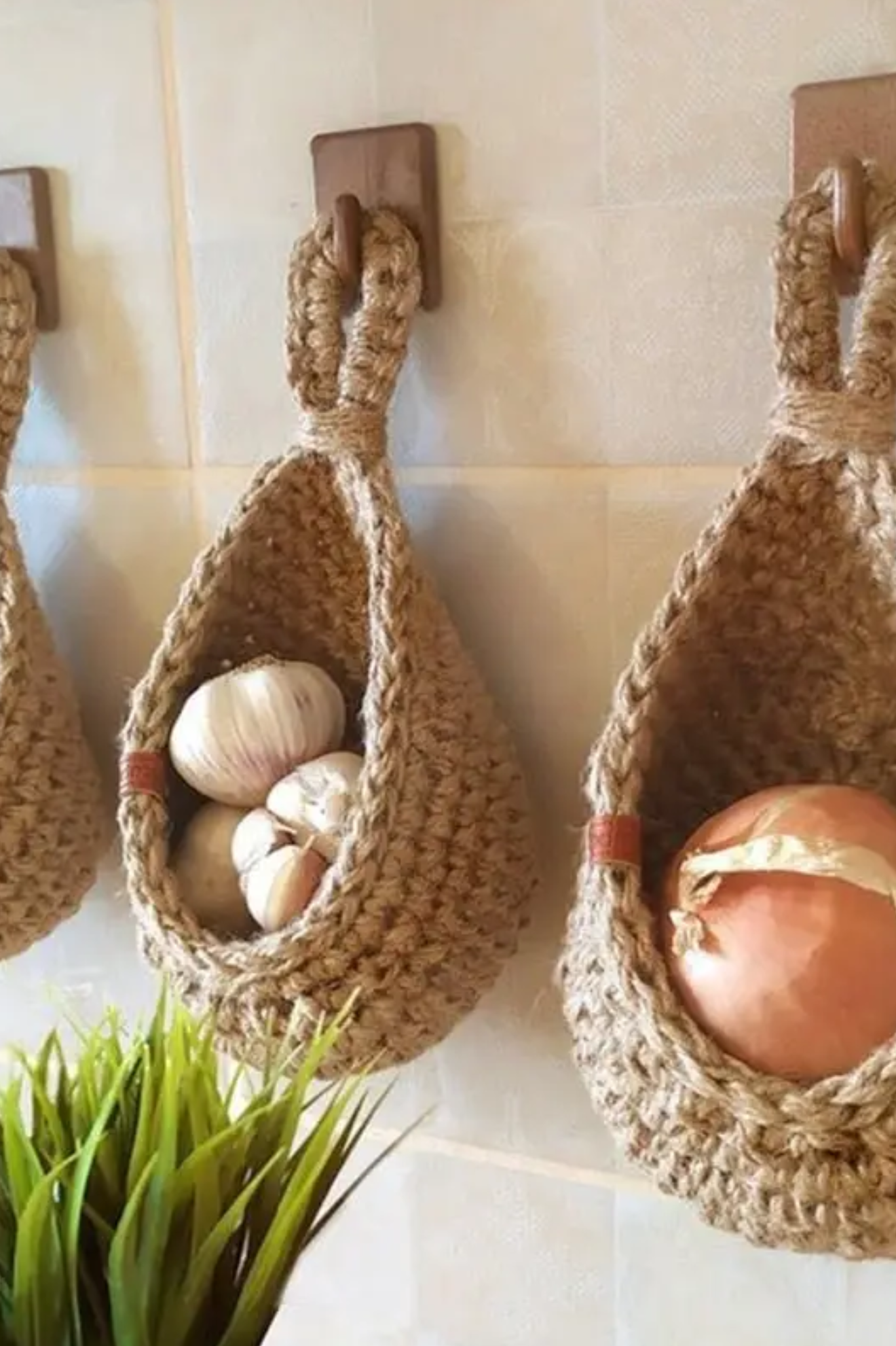Woven baskets hanging on a tiled wall with garlic and onions inside.