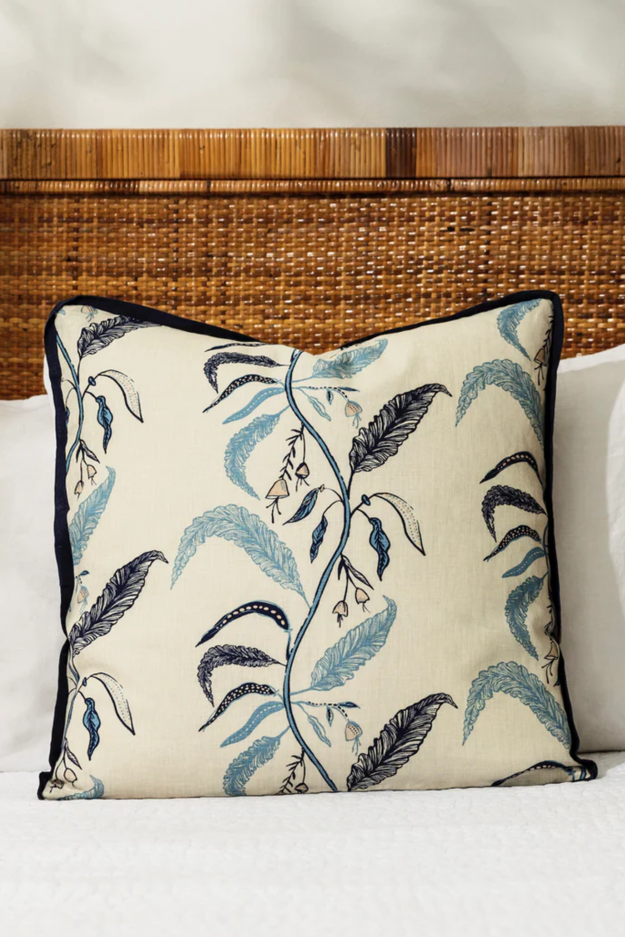 Decorative pillow with leaf pattern on a bed with wicker headboard