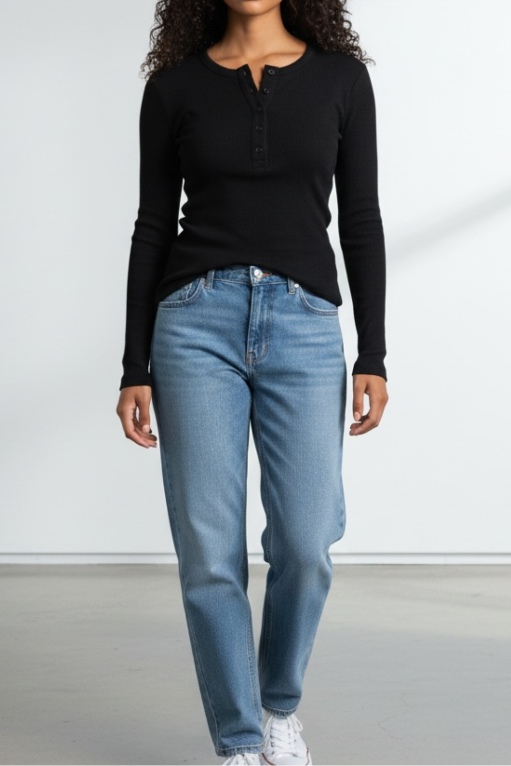 Woman wearing a black long-sleeve top and blue jeans against a white background