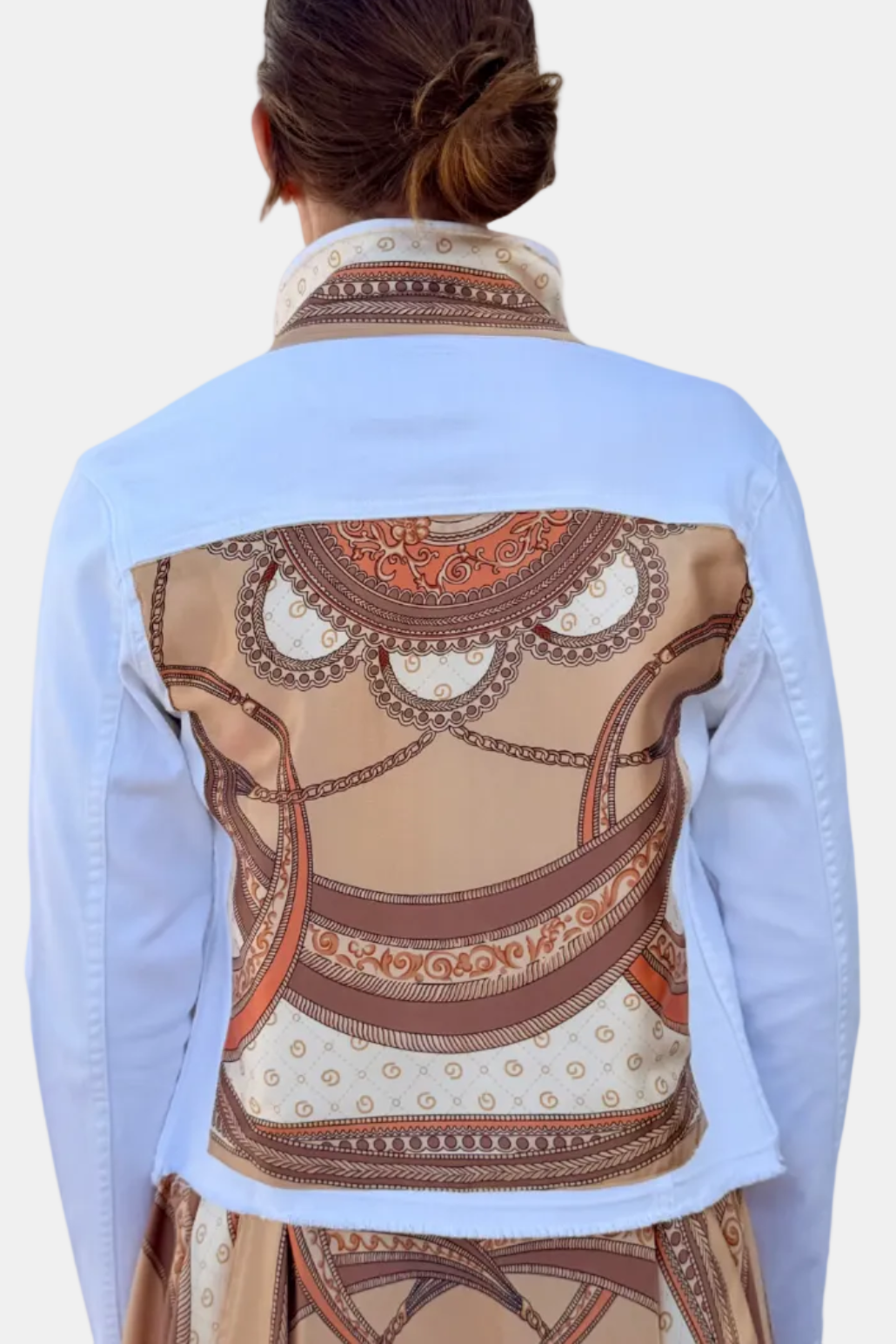 Person wearing a light blue denim jacket with a decorative pattern on the back, on a white background.