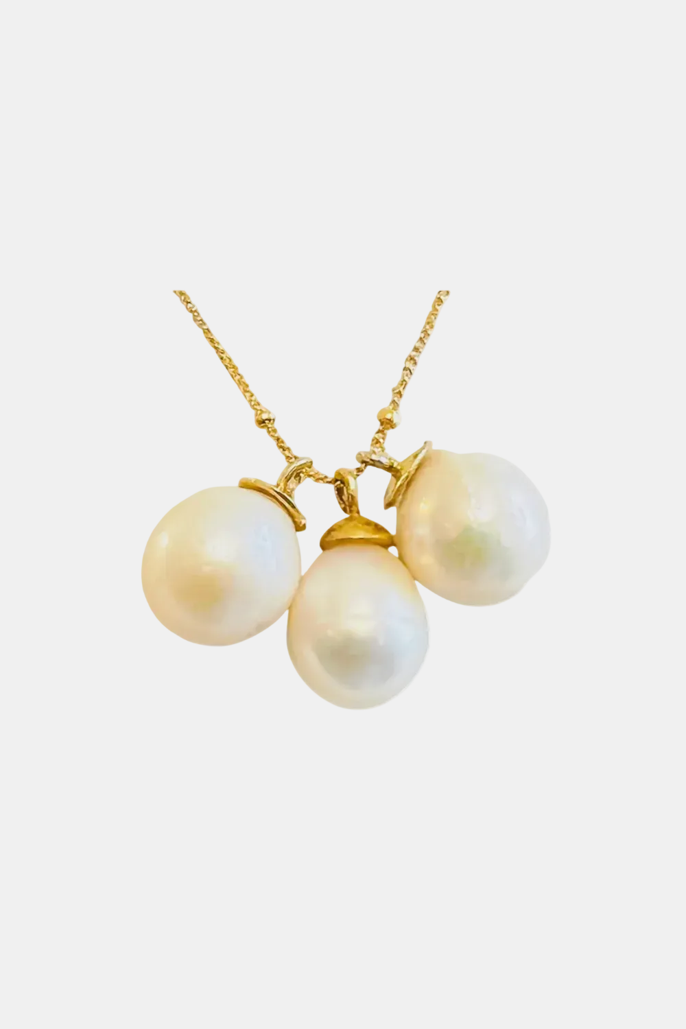 A gold necklace featuring three large, irregular white freshwater pearls suspended from a delicate gold chain against a plain white background.