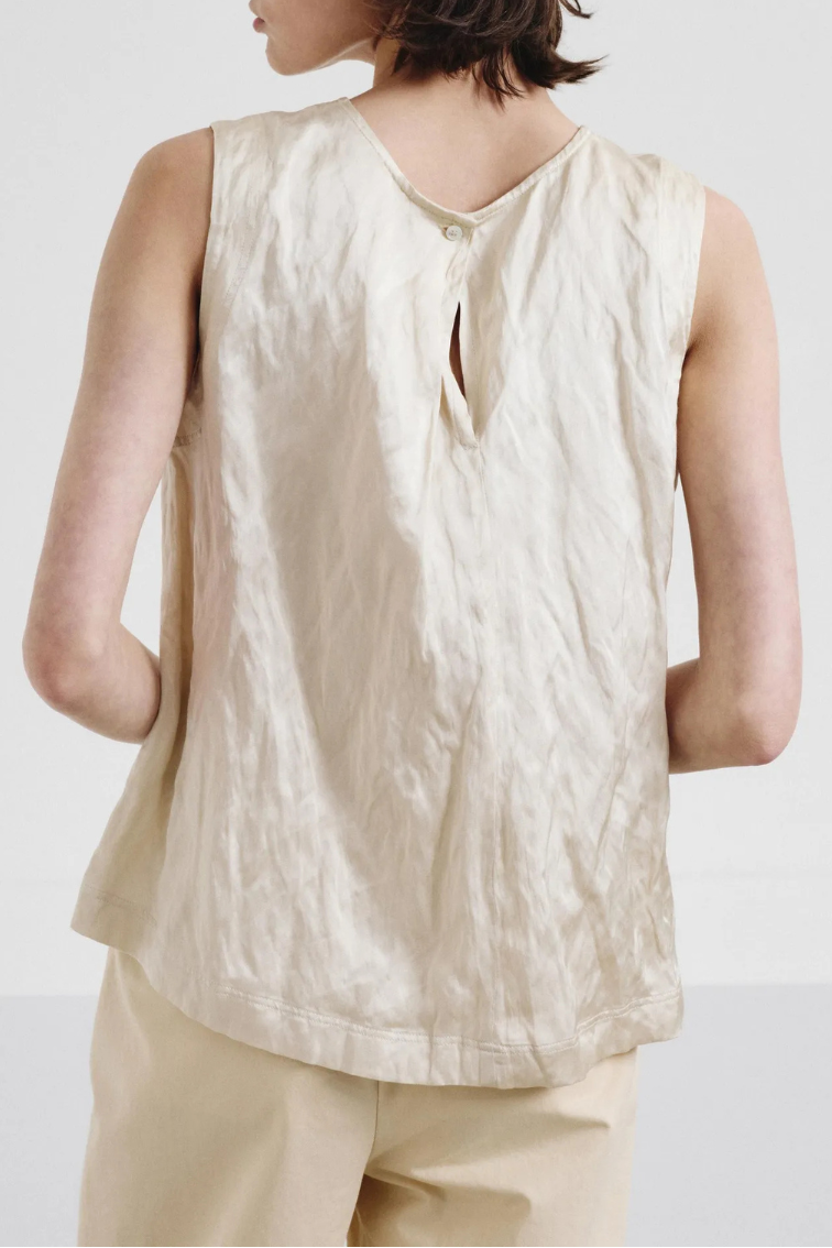 A woman shown from the back wearing a sleeveless cream-colored top with a textured crinkled fabric and a keyhole back detail, paired with matching cream trousers, set against a plain light gray background.